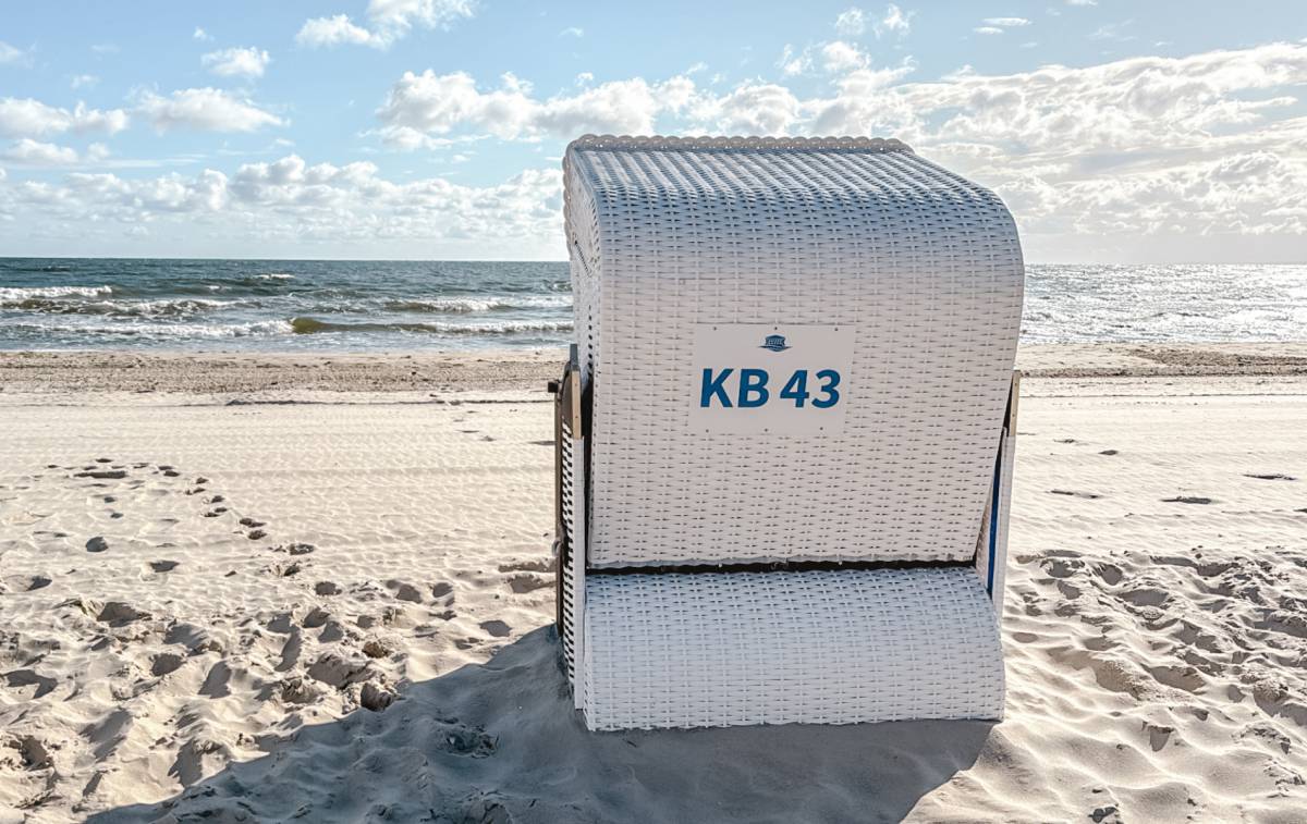 Weißer Strandkorb mit der Kennzeichnung KB 43 am Ostseestrand auf Usedom mit Meer und blauem Himmel im Hintergrund.