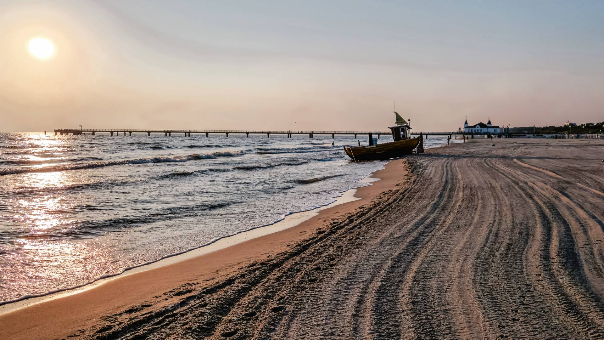 Strand von Ahlbeck auf Usedom bei Sonnenaufgang mit Seebrücke, sanften Wellen und einem Fischerboot im Sand