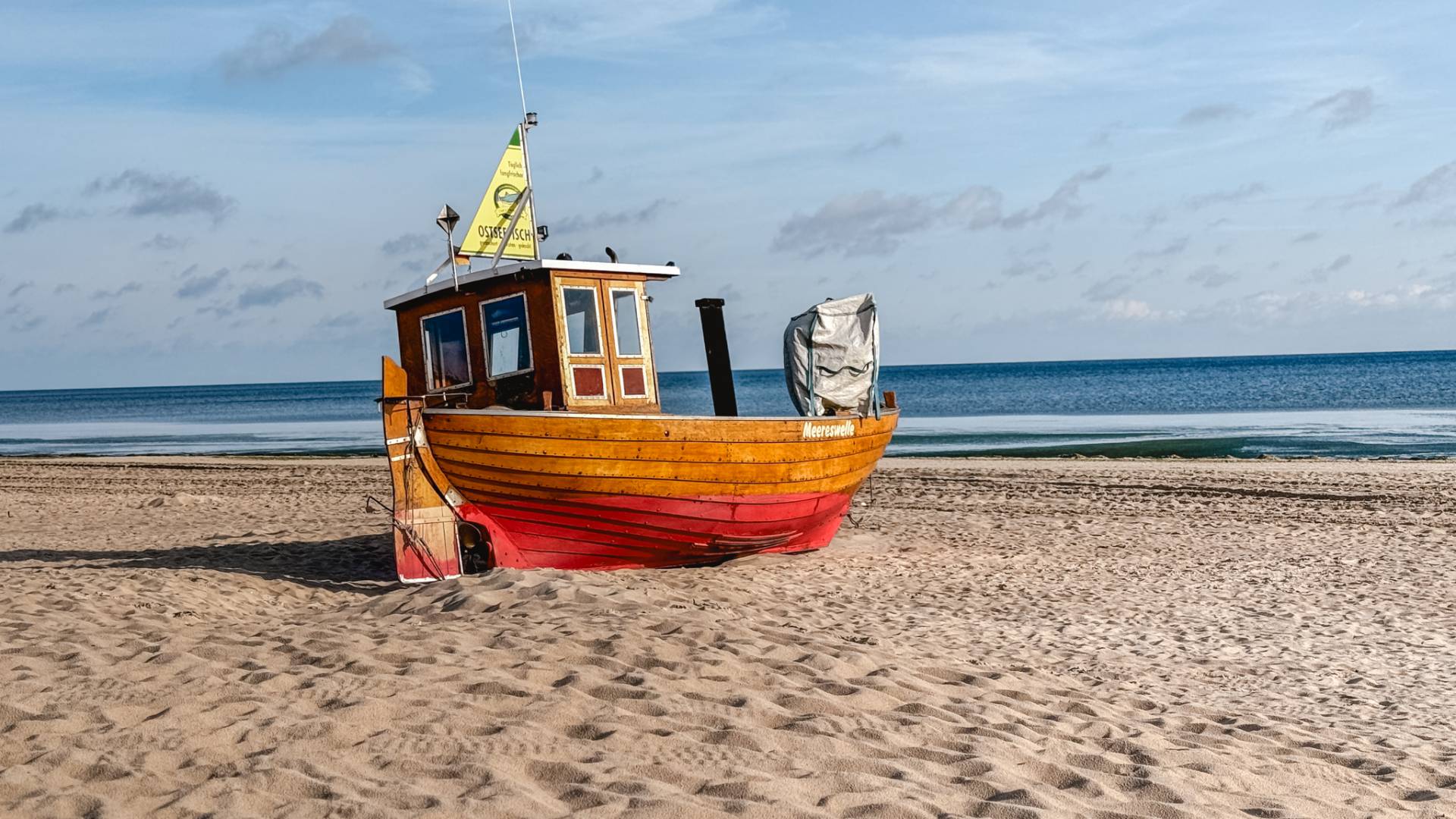 Holz-Fischerboot am Strand der Ostsee auf Usedom, direkt am Wasser gelegen, bei ruhigem Meer und blauem Himmel