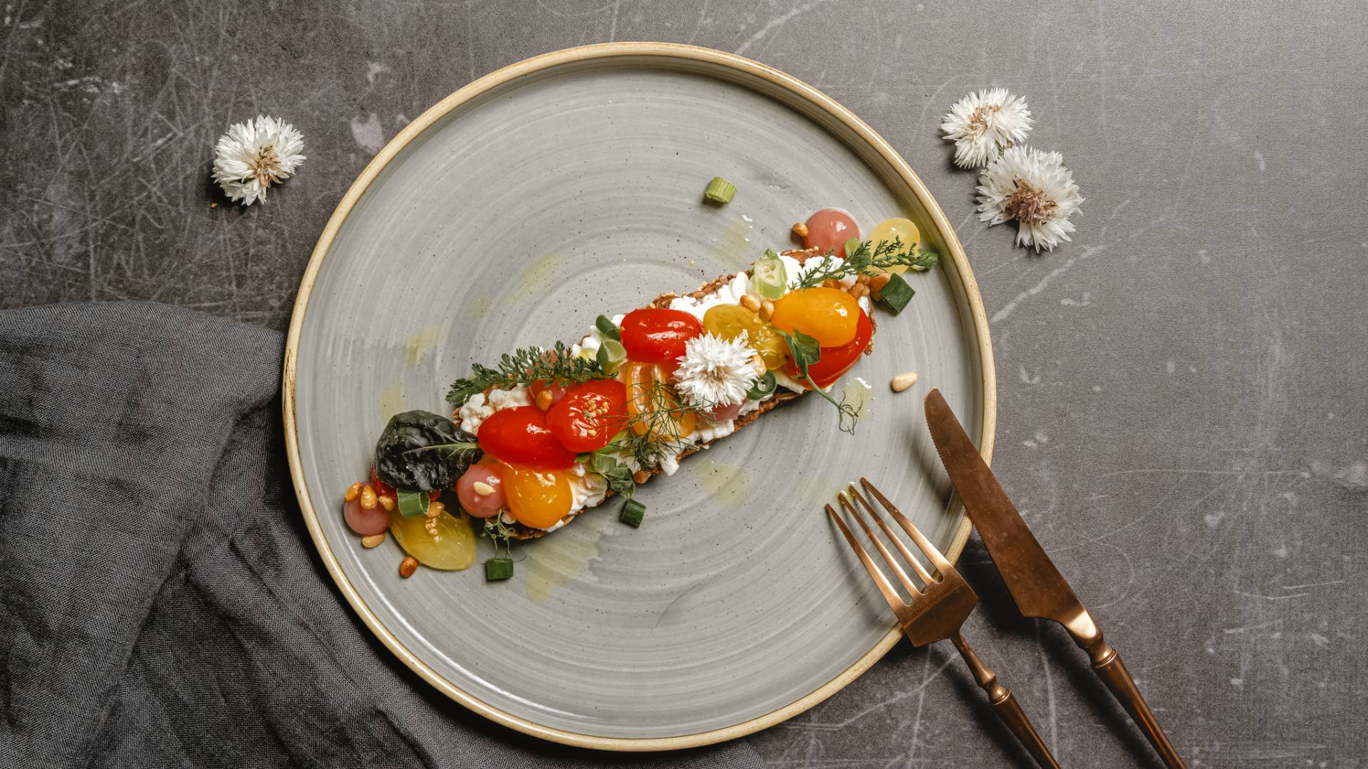 Bruschetta mal anders, Geröstetes Vollkornbrot vom AHLBÄCKER, eingelegten Cherrytomaten, körniger Frischkäse, gerösteten Pinienkerne, fruchtiges Pfirsichgel und Lauchzwiebeln im Restaurant Düne 48