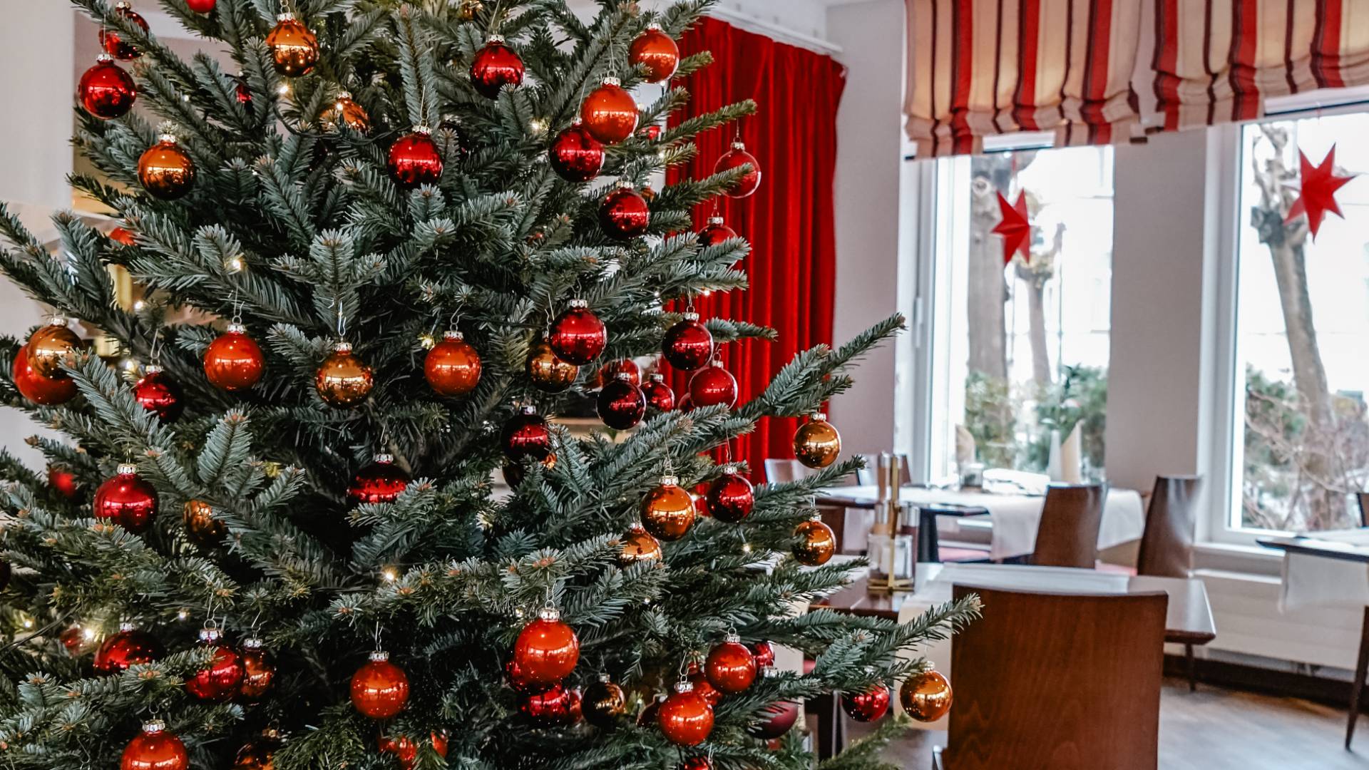 Weihnachtsbaum mit roten Kugeln im Vordergrund und eingedeckte Tische und Stühle mit Fenster vom Restaurant Düne 48