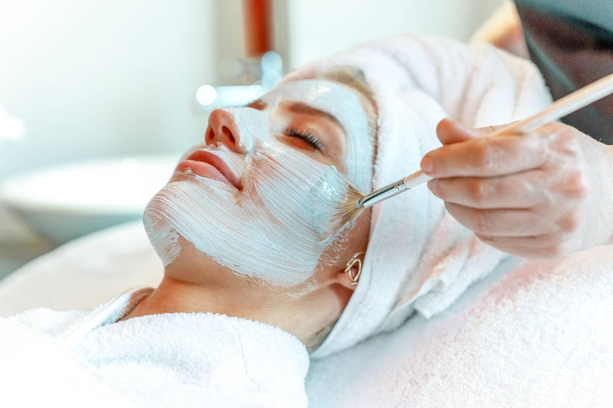 Entspannte Frau erhält im Spa eine professionelle Gesichtsbehandlung, während eine Pflegemaske mit einem Pinsel aufgetragen wird