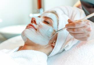 Entspannte Frau erhält im Spa eine professionelle Gesichtsbehandlung, während eine Pflegemaske mit einem Pinsel aufgetragen wird