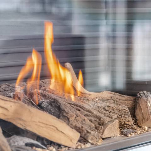 Moderner Kamin im Hotelzimmer mit lodernden Flammen und Holzdekor hinter Glasscheibe