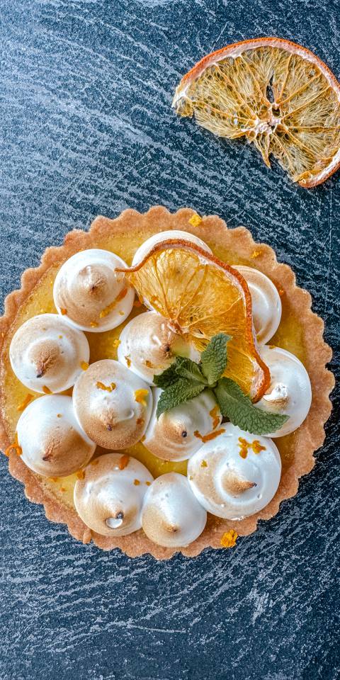 Feines Orange-Baiser-Tartelette mit cremiger Orangenfüllung und getoastetem Baiser, dekoriert mit getrockneter Orangenscheibe und Minze im Günter’s im DAS AHLBECK HOTEL & SPA