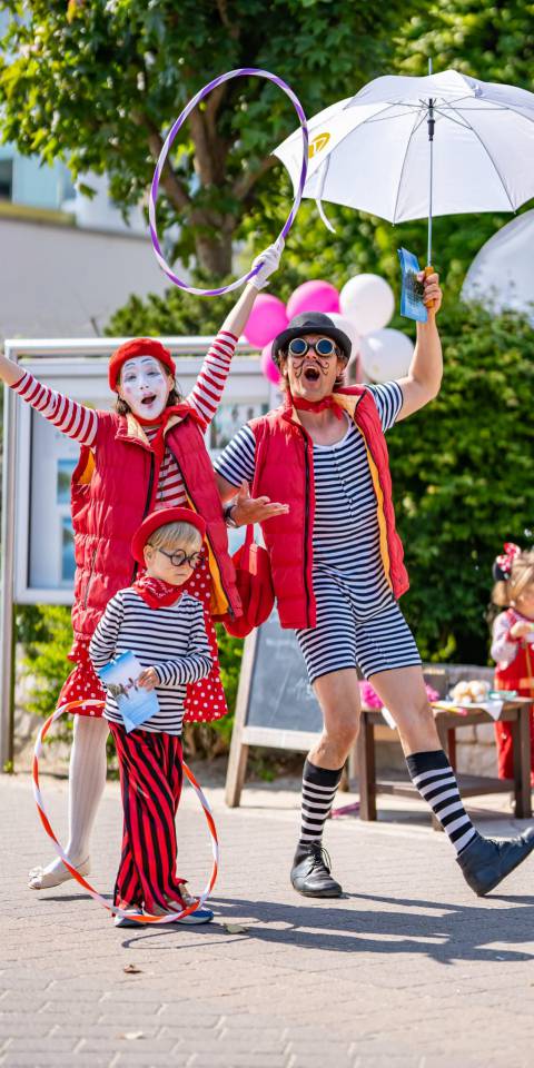 Bunte Clowns und ein verkleidetes Kind sorgen bei einem Familienevent im Freien für fröhliche Stimmung
