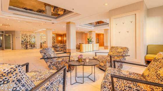 Hotellobby DAS AHLBECK HOTEL & SPA mit Schwingsesseln, Blumengesteck auf goldenem Sideboard als Dekoelement