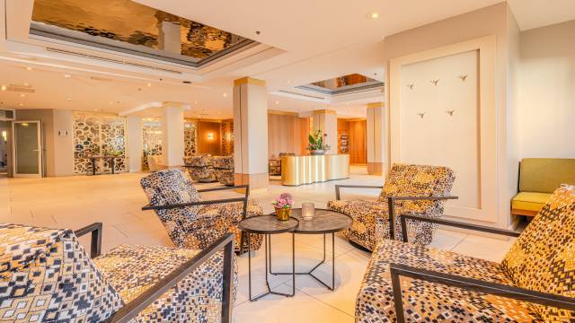 Hotellobby DAS AHLBECK HOTEL & SPA mit Schwingsesseln, Blumengesteck auf goldenem Sideboard als Dekoelement