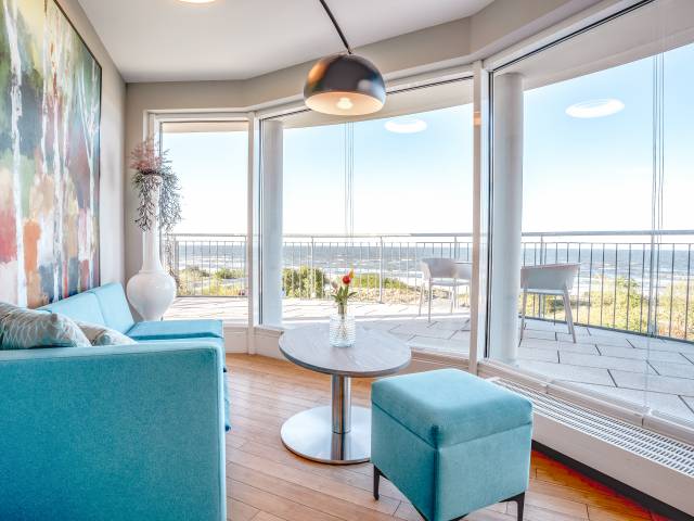 Helles Zimmer im Das Ahlbeck Hotel & Spa mit modernem Sofa, bodentiefen Fenstern und Panoramablick auf die Ostsee vom Balkon