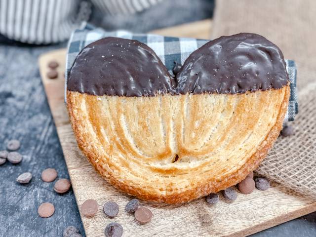 Knuspriges Schweineohr vom DER AHLBÄCKER – zartes Blätterteiggebäck, teilweise mit dunkler Schokolade überzogen.