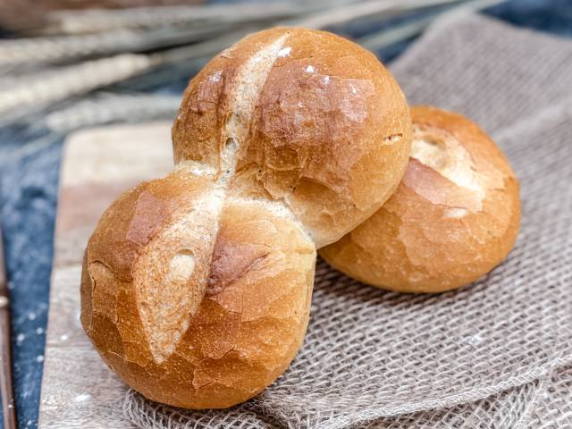 Zwei frisch gebackene, goldbraune doppelte Weizenbrötchen vom DER AHLBÄCKER auf Leinentuch angerichtet