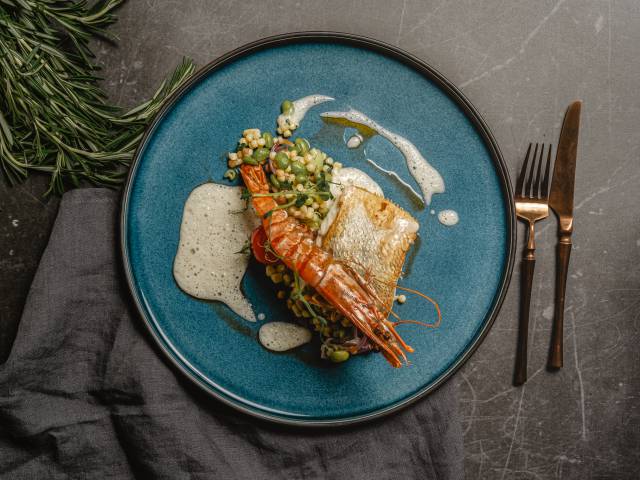Gebratenes Zanderfilet mit Garnele als Gourmetgericht im Restaurant Düne 48, angerichtet auf einem blauen Teller mit Gemüse und feiner Sauce