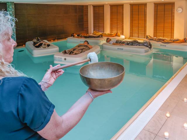 Schwebendes Klangbad Floating Soundbath, 5 Teilnehmer treiben schwerelos auf Luftbetten im warmen Wasser während die Klangschalen und der Gong angeschlagen werden