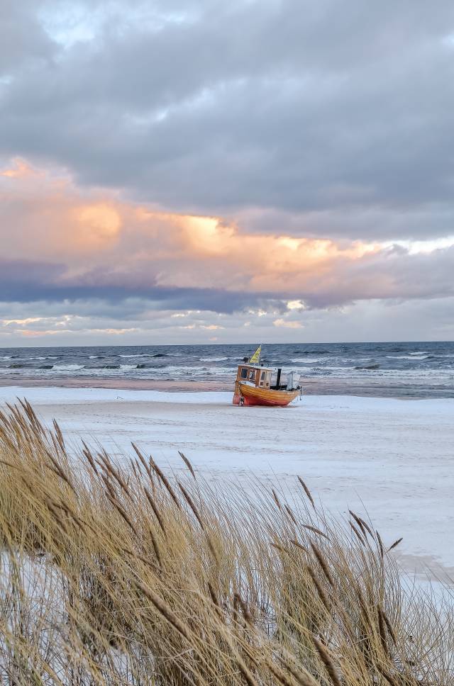 Winterlicher Strand von Ahlbeck auf Usedom mit Fischerboot am Ostseestrand und Dünen im Vordergrund unter wolkigem Himmel