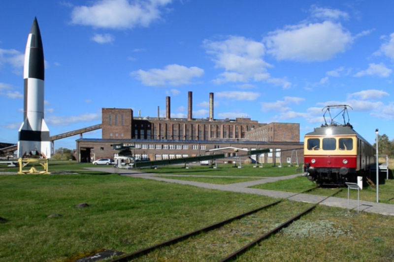 Außenansicht des Historisch-Technischen Museums Peenemünde auf Usedom mit historischer Lokomotive und Rakete auf dem Freigelände vor dem Backsteingebäude