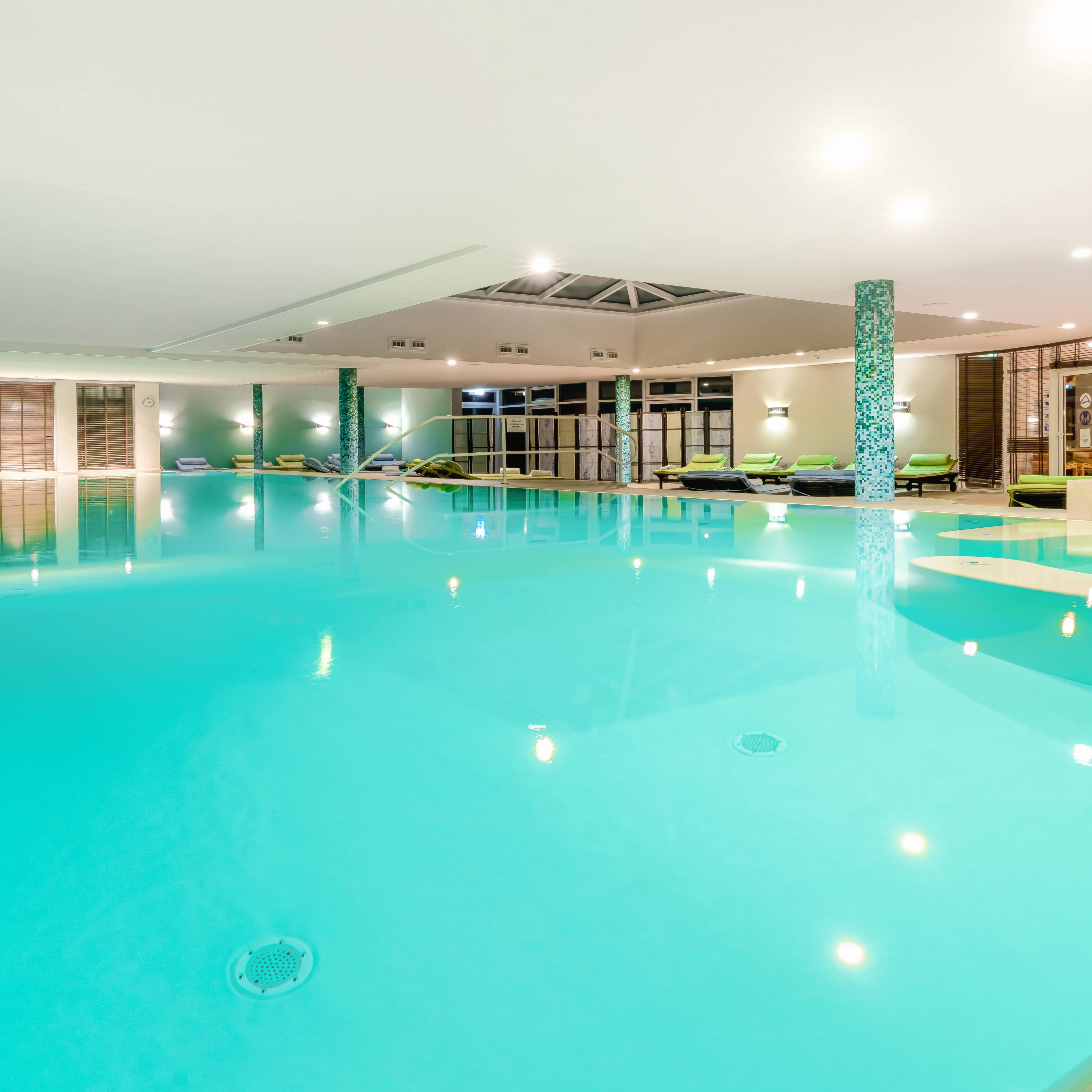 Großzügiger 25-Meter-Indoorpool im Familien SPA des Das Ahlbeck Hotel & Spa****S mit Liegebereich und stimmungsvoller Beleuchtung