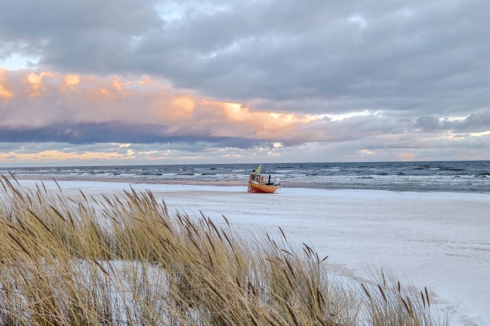 Winterlicher Strand von Ahlbeck auf Usedom mit Fischerboot am Ostseestrand und Dünen im Vordergrund unter wolkigem Himmel