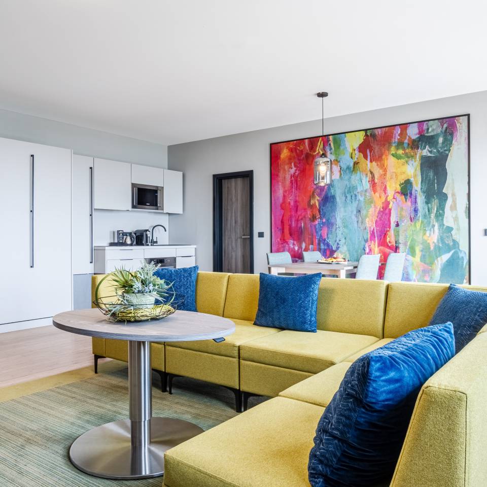 Modern eingerichtetes Zimmer im Das Ahlbeck Hotel & Spa mit großer Couch, Küchenzeile und farbenfrohem Wandbild
