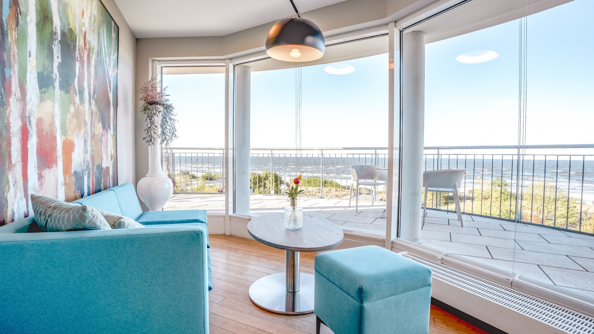 Helles Zimmer im Das Ahlbeck Hotel & Spa mit modernem Sofa, bodentiefen Fenstern und Panoramablick auf die Ostsee vom Balkon