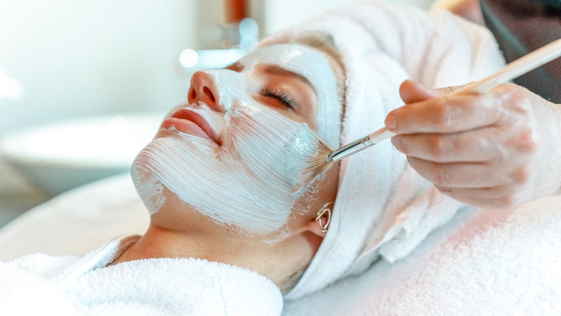 Entspannte Frau erhält im Spa eine professionelle Gesichtsbehandlung, während eine Pflegemaske mit einem Pinsel aufgetragen wird